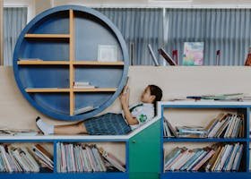 A young girl in a school uniform relaxes and reads in a modern library setting.