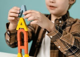 Young boy stacking colorful alphabet blocks on table indoors.